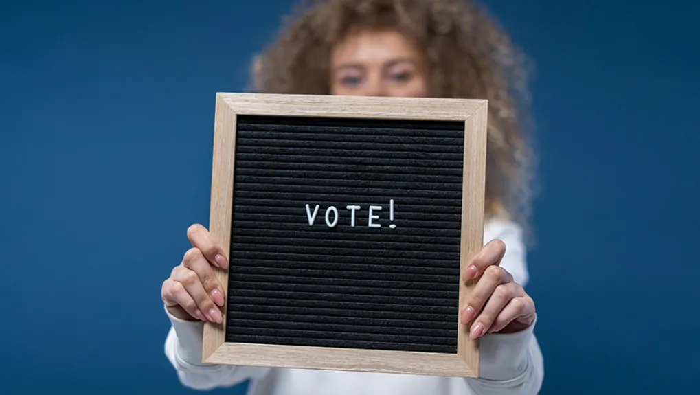 Een vrouw die een bord ophoudt met daarop: Vote!