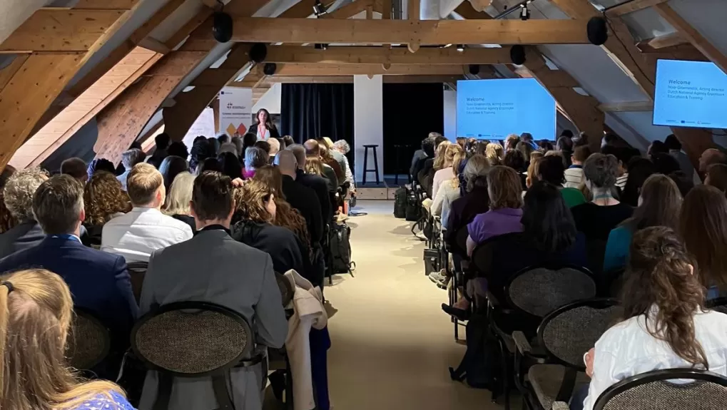 Foto van achteren tijdens een plenaire sessie tijdens de TCA. Je ziet Noor Groenendijk vooraan spreken, en kijkt bij de deelnemers op de rug. Ze zitten in rijen, met een pad in het midden als doorbreking.