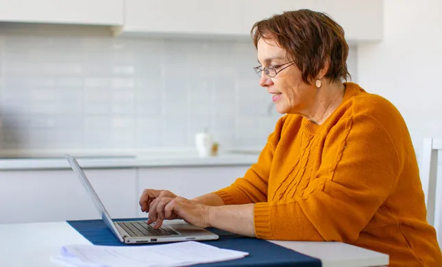 Oudere vrouw achter een laptop, bezig met een inschrijving