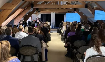 Foto van achteren tijdens een plenaire sessie tijdens de TCA. Je ziet Noor Groenendijk vooraan spreken, en kijkt bij de deelnemers op de rug. Ze zitten in rijen, met een pad in het midden als doorbreking.
