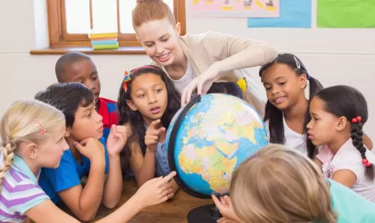 Kinderen uit een basisschoolklas staan om een wereldbol heen, de docent wijst iets aan op de wereldbol