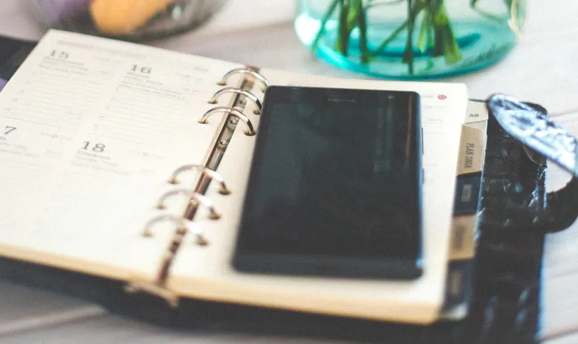 Een opengeslagen papieren agenda plus telefoon op tafel