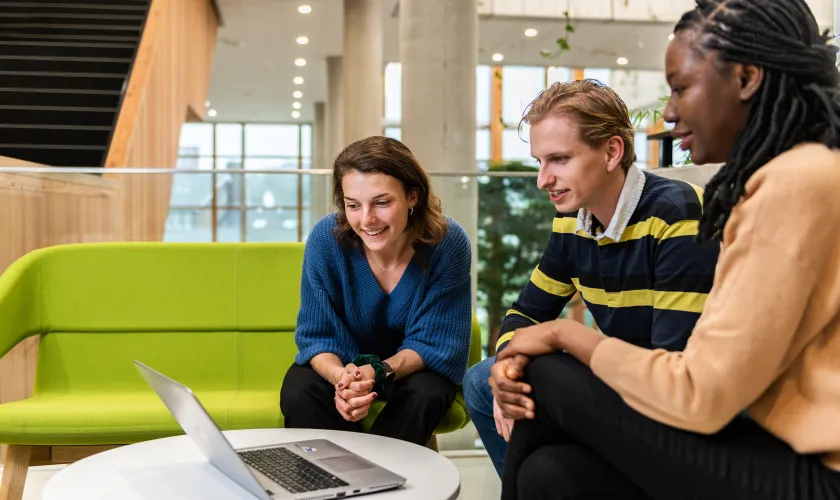 Drie jonge mensen kijken naar een laptop